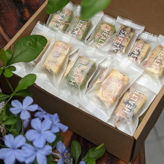Hộp kraft mở nắp xếp những viên Kẹo Hạnh Phúc gói riêng, bên cạnh nhành hoa xanh lam